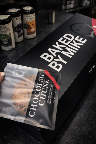 Editorial product photo of Baked by Mike chocolate chunk cookie packaging featuring a custom printed mylar cookie bag and premium bakery box designed by Cheetah Pak Packaging & Design.