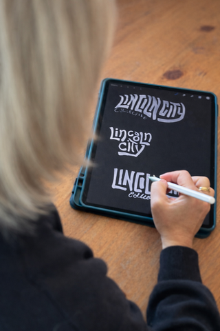 Designer using a stylus on an iPad with 'Lincoln City' branding.