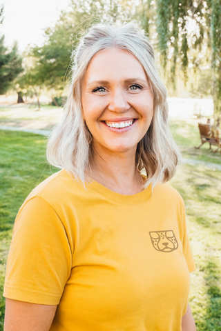 Graphic Designer headshot in Southern Oregon wearing a yellow t-shirt with a Cheetah Pak logo, standing outdoors in a park-like setting.